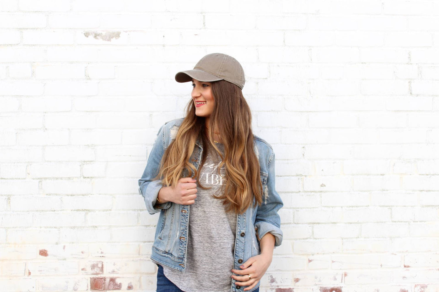 woman leaning against white wall in baseball cap